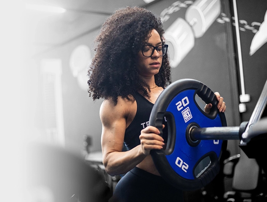 Growth Supplements - atleta mulher segurando anilha azul de 20 kg na academia