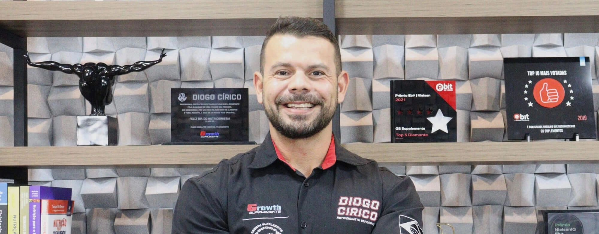 Retrato de Diogo Círico, nutricionista esportivo, em escritório com prateleiras com troféus