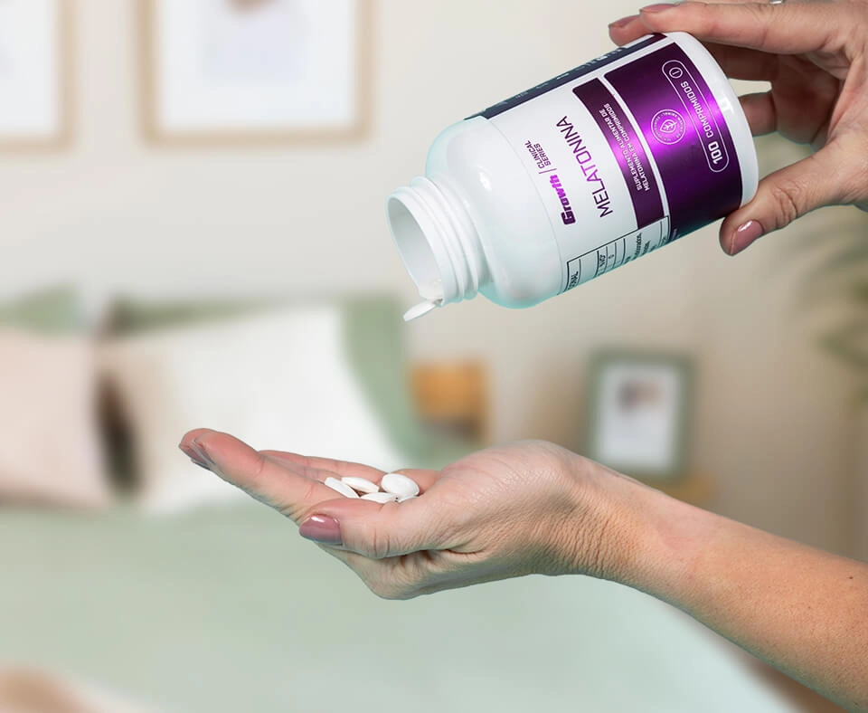 Uma mão esquerda de uma mulher com comprimidos na mão, e na mão direita a embalagem da melatonina 0,21mg (100 Comprimidos) - Growth Supplements
