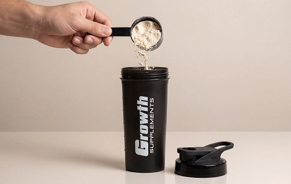 A mão de uma pessoa segurando um scoop com o pó do produto growth supplements, e uma coqueteleira Growth Supplements abaixo.